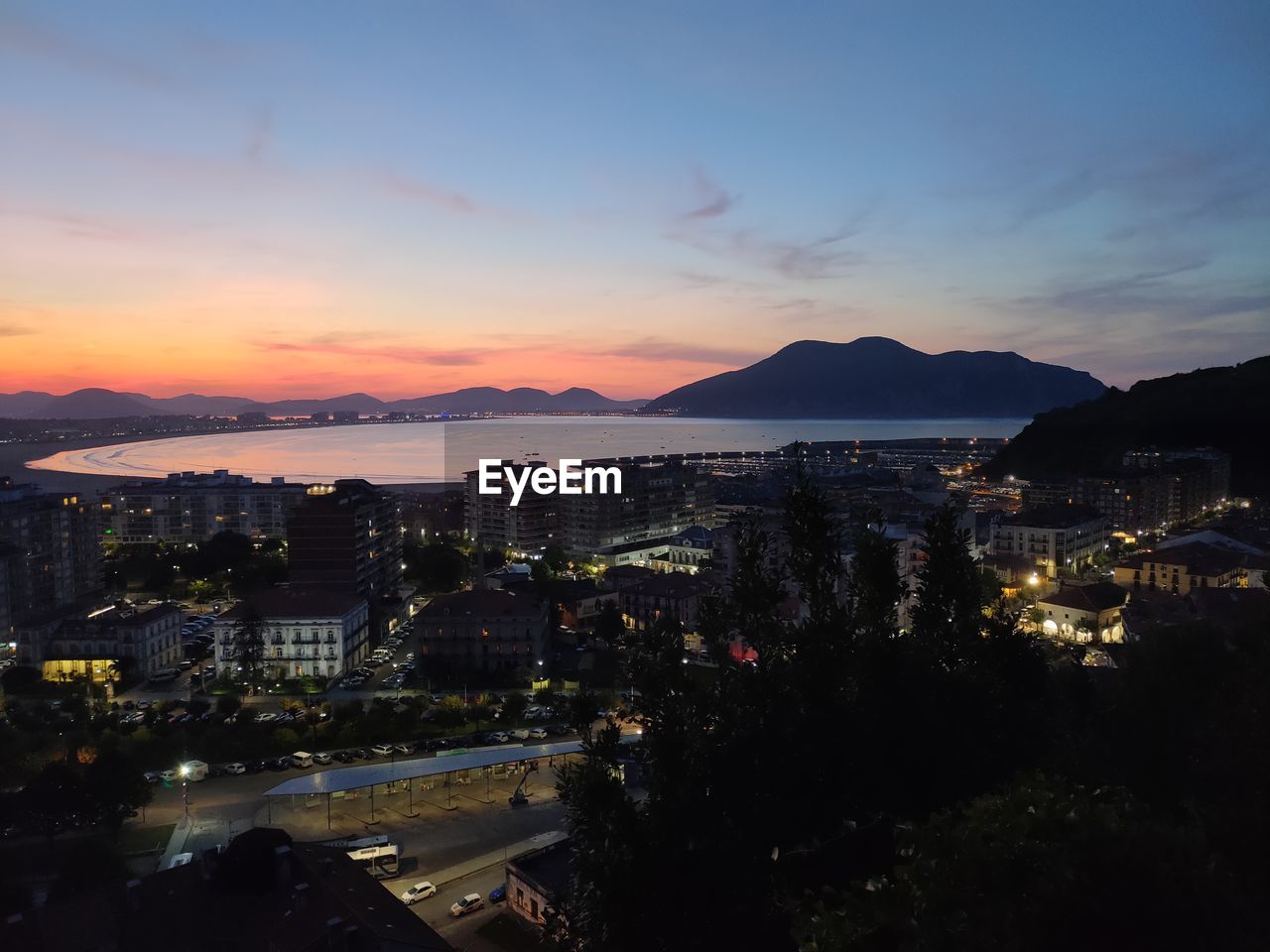 High angle view of illuminated city by sea against sky