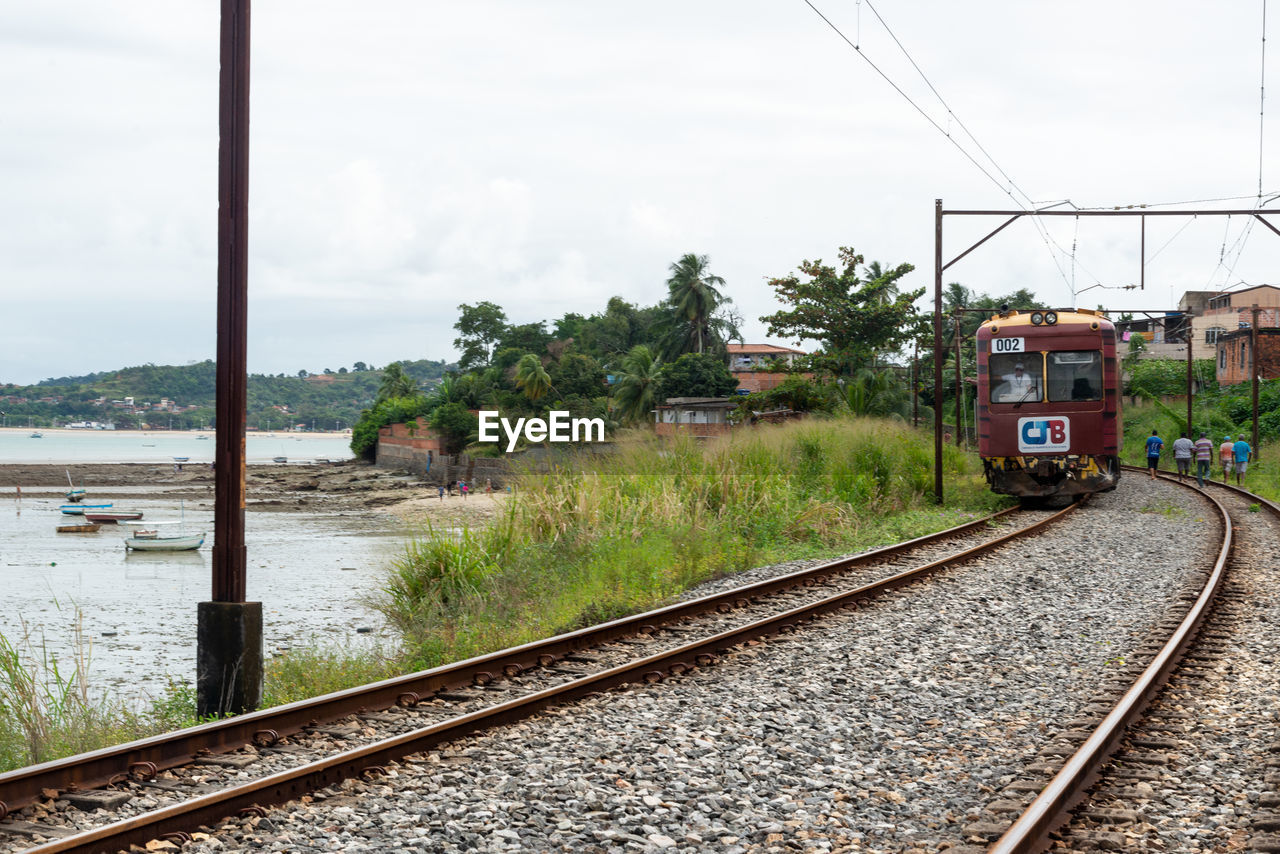 transportation, rail transportation, railroad track, track, mode of transportation, sky, railway, transport, public transportation, nature, vehicle, train, travel, cloud, architecture, water, no people, day, plant, electricity, cable, outdoors, tree, land vehicle, residential area, travel destinations, locomotive, rolling stock, power line