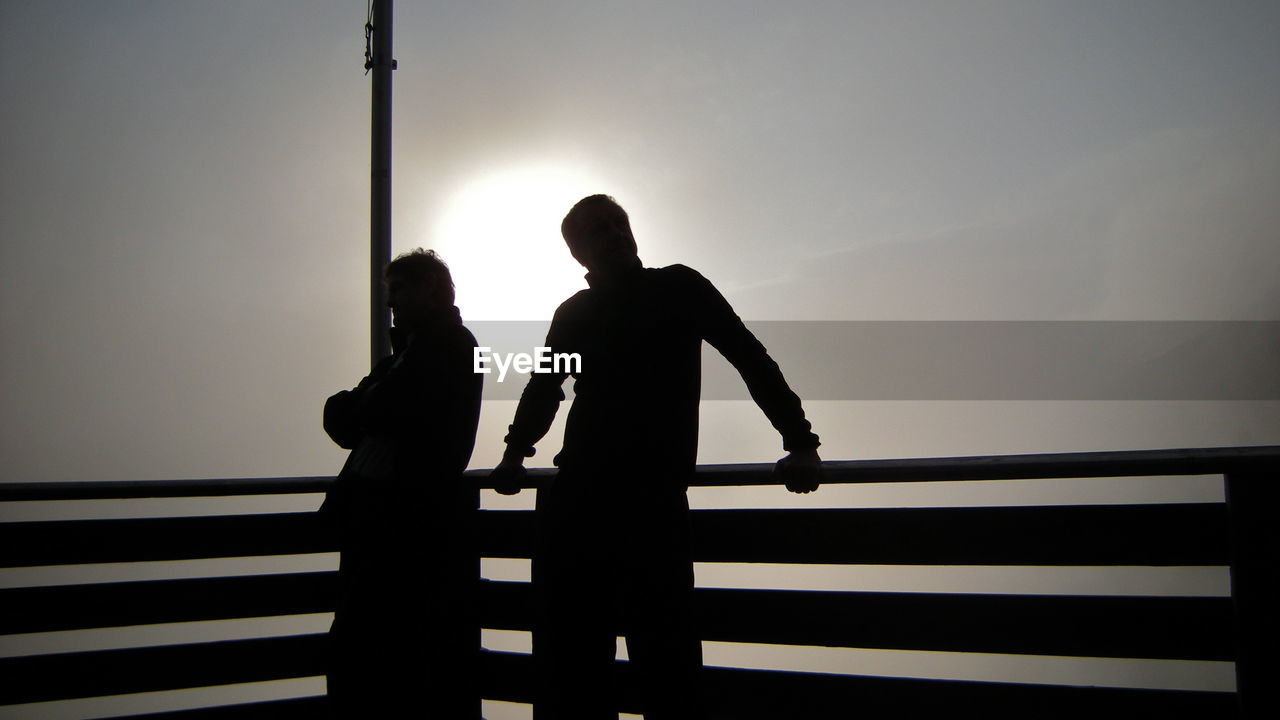 Silhouette of people on railing against sky