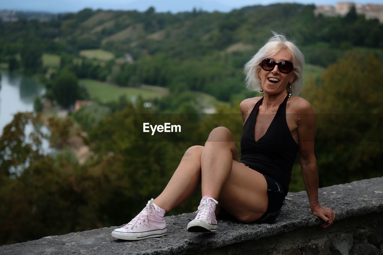 Happy woman sitting on rock against trees