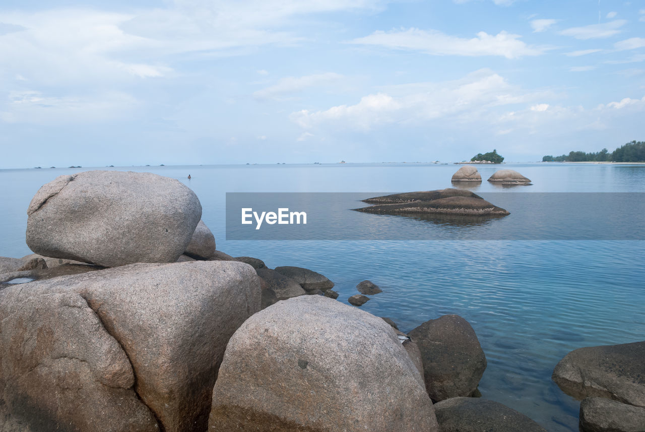 Rocks on beach against cloudy sky