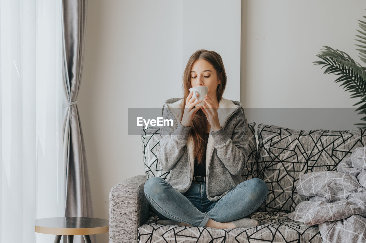 Young woman drinking coffee sitting on sofa at home
