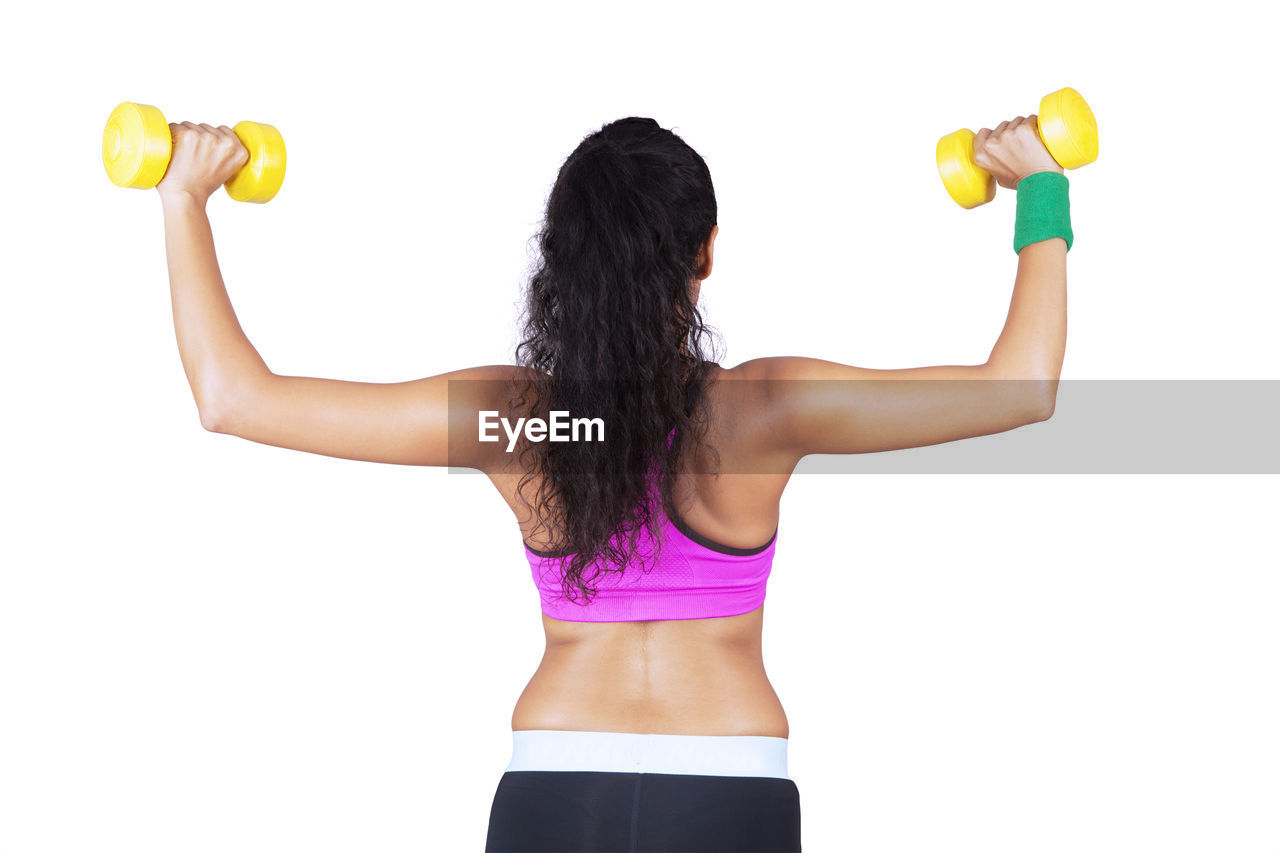 Rear view of woman exercising with dumbbells against white background