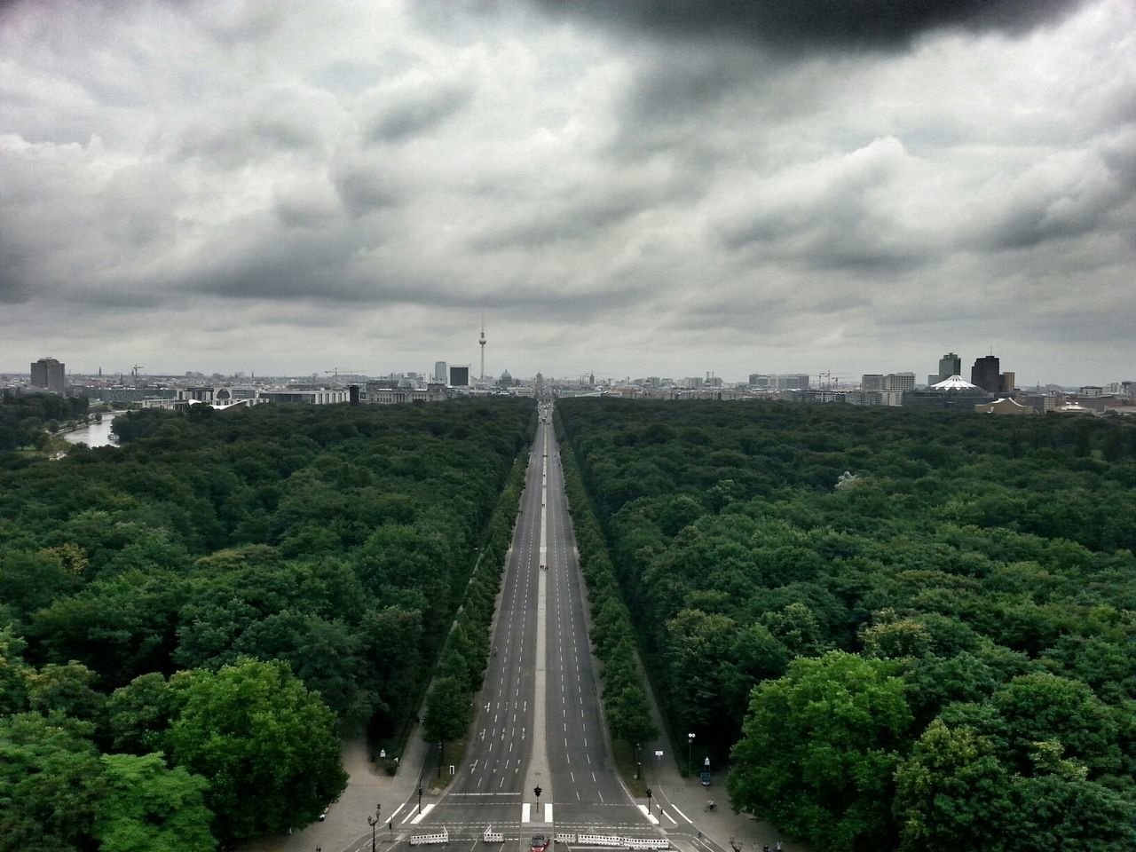 Aerial view of long highway between dense forests against cloudy sky