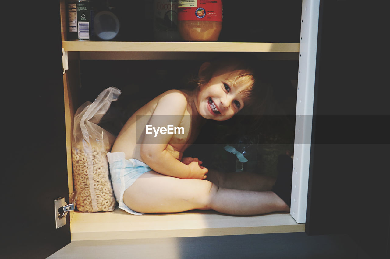Cute little girl hiding inside kitchen cabinet
