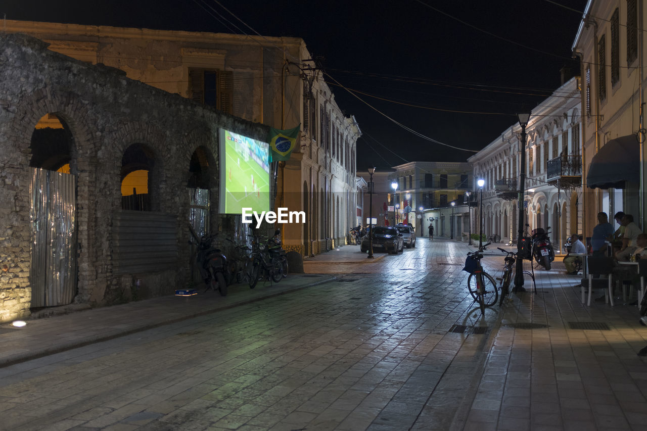 PEOPLE ON STREET AMIDST BUILDINGS AT NIGHT