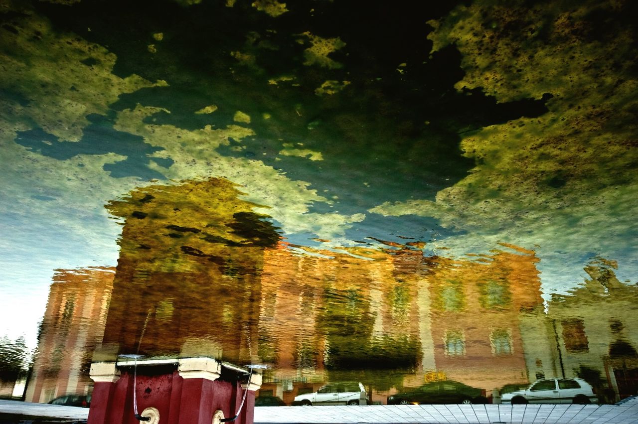 Reflection of building against cloudy sky on puddle