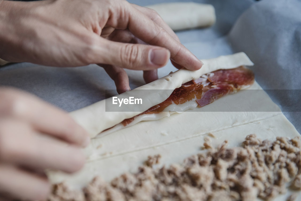 Crop person making meat rolls person
