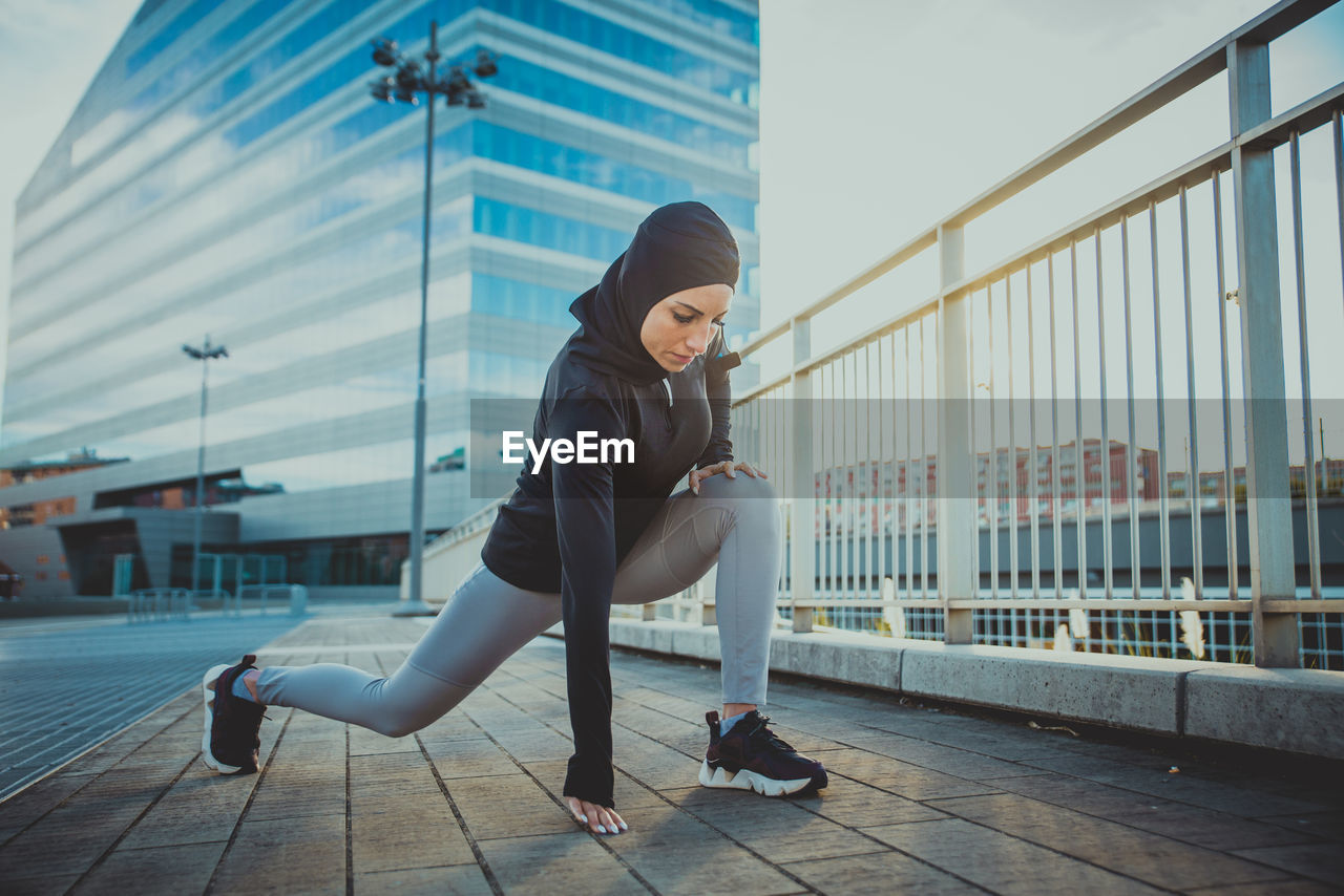 Beautiful woman wearing hijab exercising against building during sunrise