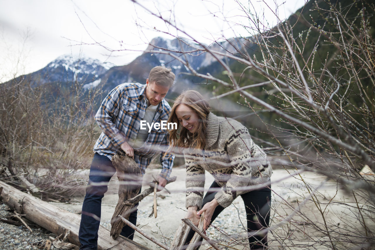 Young couple collecting wood for campfire against mountains