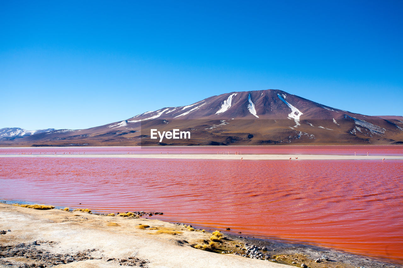 Scenic view of red lake and mountains against clear blue sky