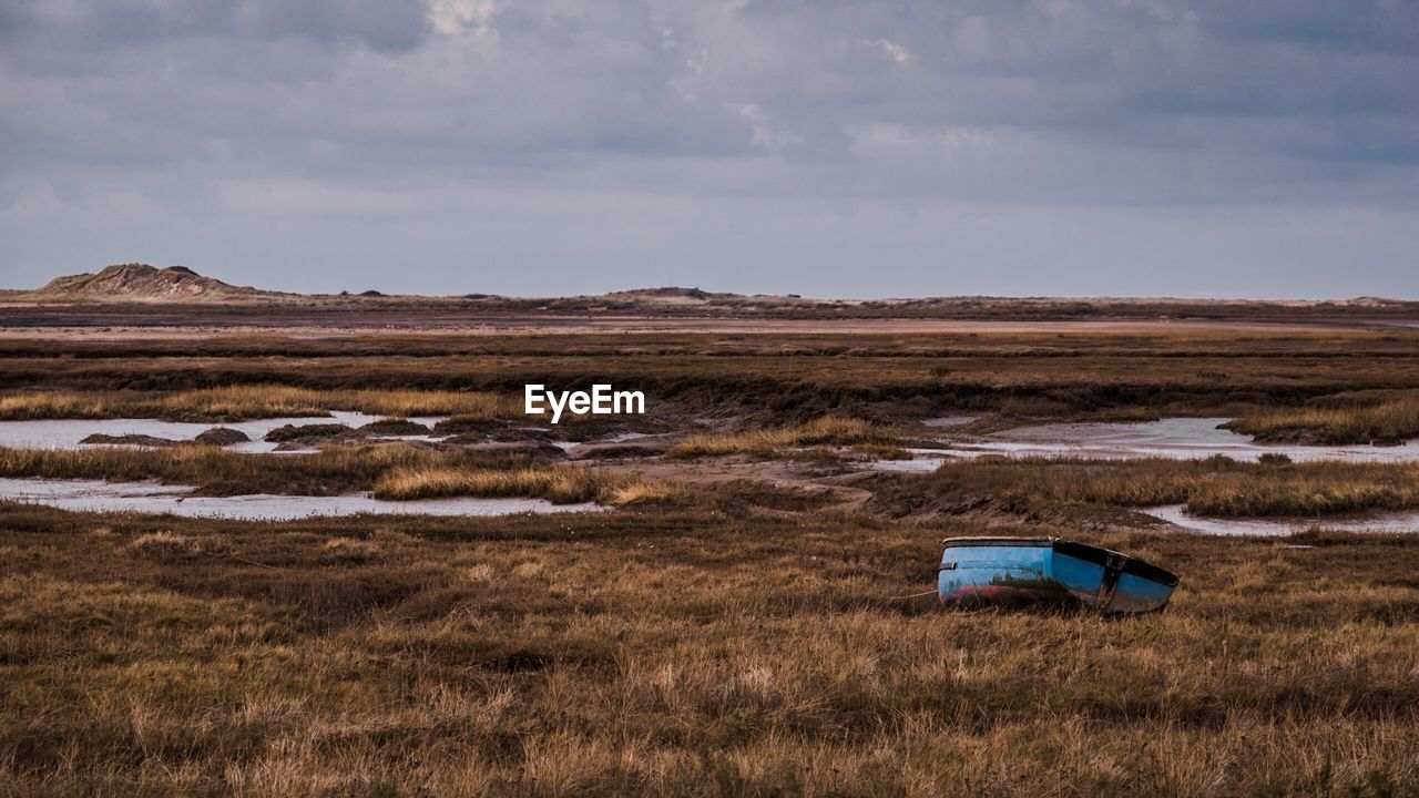 Abandoned boat on grassy field against cloudy sky