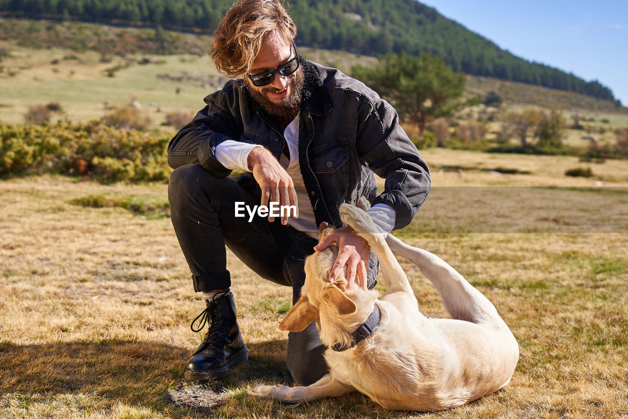 Portrait of young tattoed man playing with his dog in the countryside