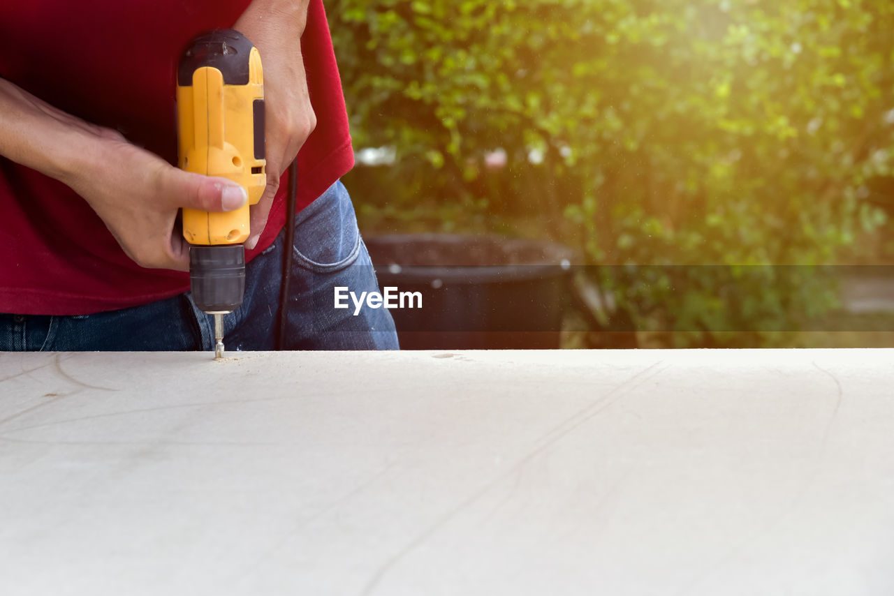 Close-up midsection of man drilling wood outdoors