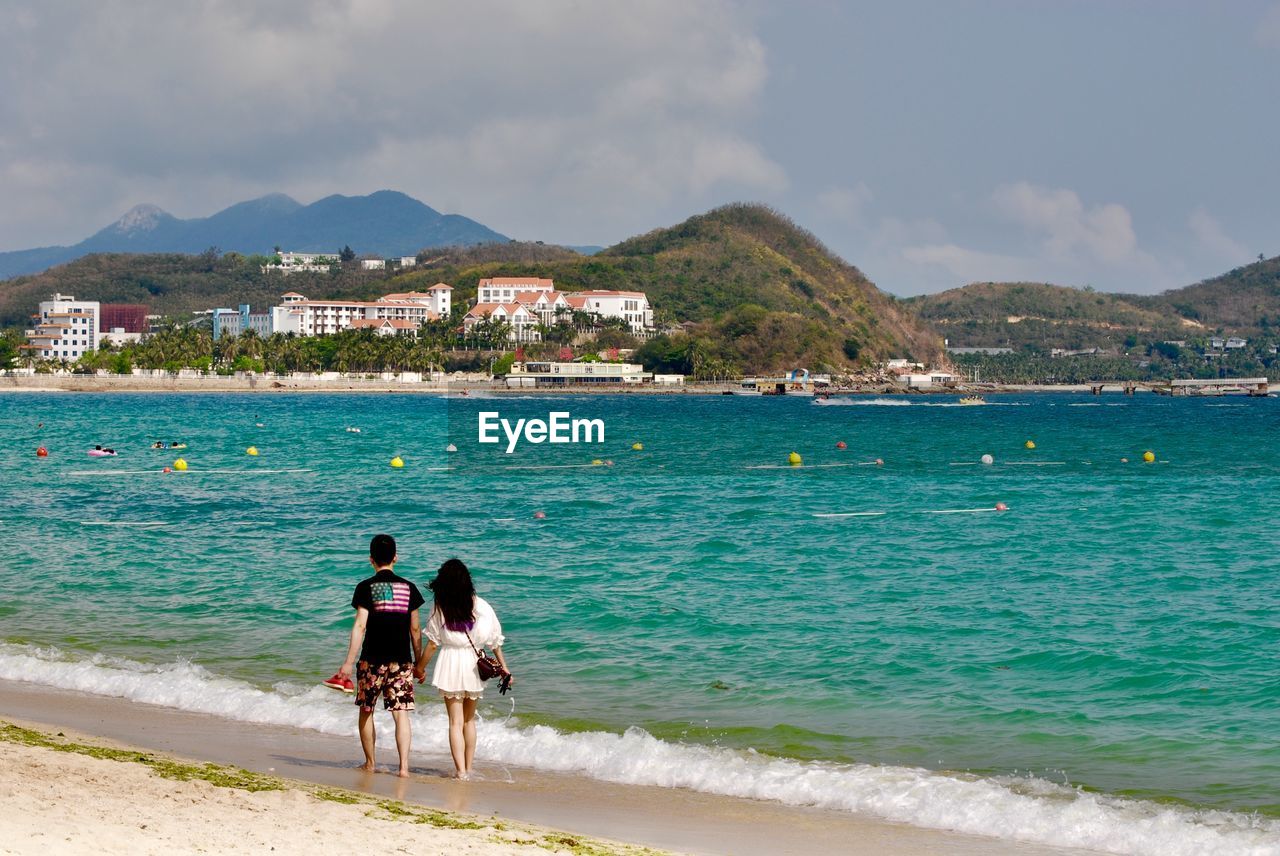 REAR VIEW OF MEN AT BEACH AGAINST SKY