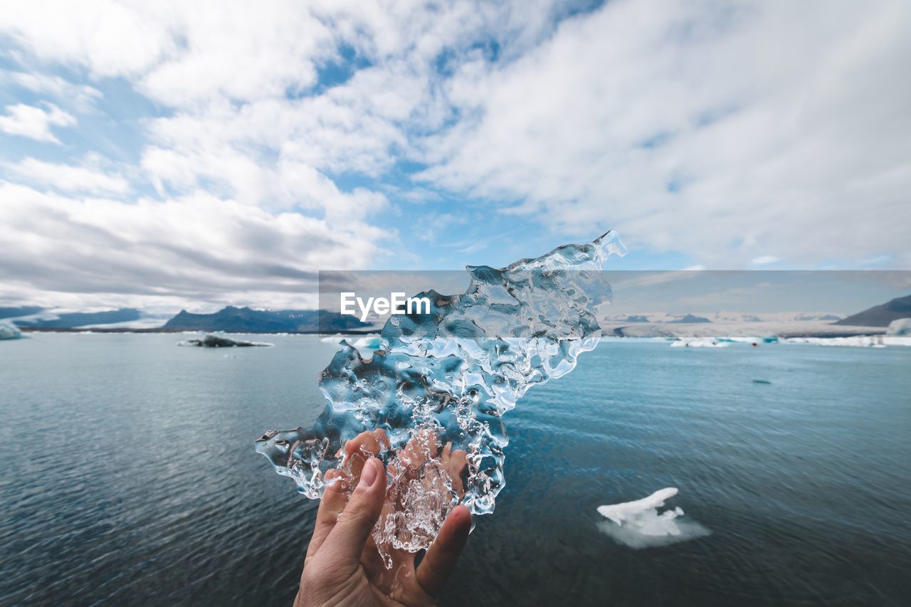 Cropped hand holding ice against sea