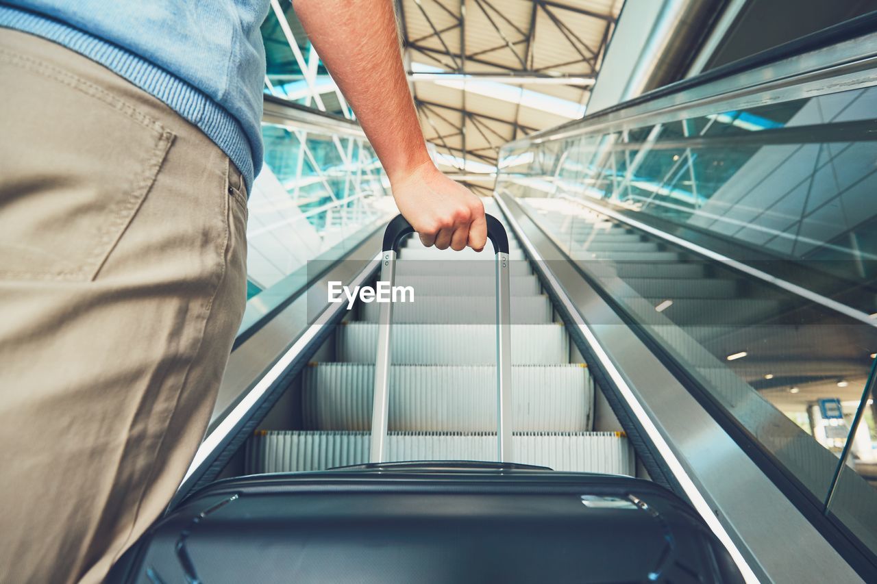 Cropped image of man holding luggage on escalator at airport
