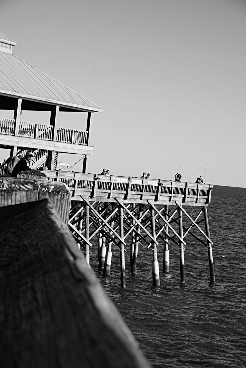 People standing on pier over sea against clear sky