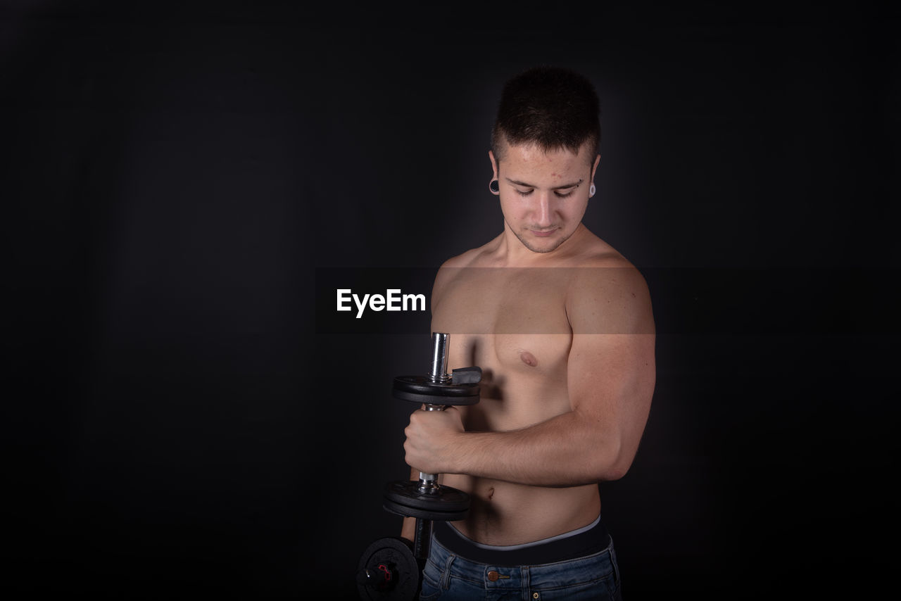 Shirtless man lifting dumbbells against black background