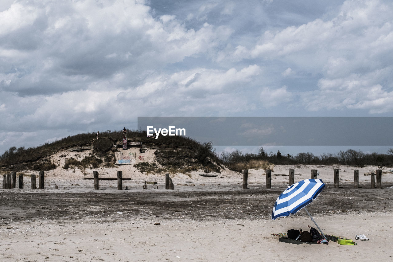 Umbrella at sandy beach against cloudy sky