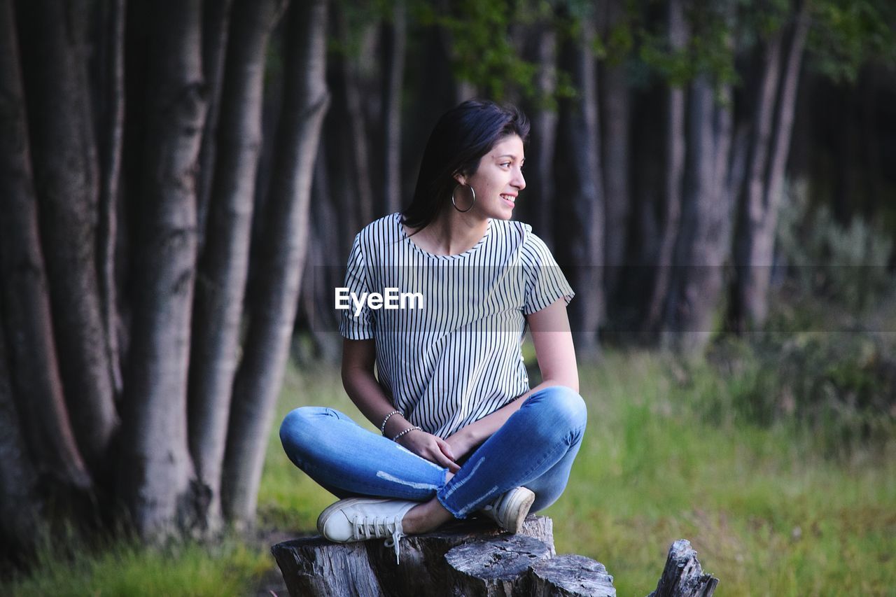 Full length of woman sitting on tree stump in forest