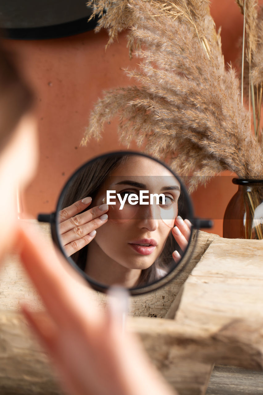 Mirror reflection of woman applying under-eye patch at dressing table closeup