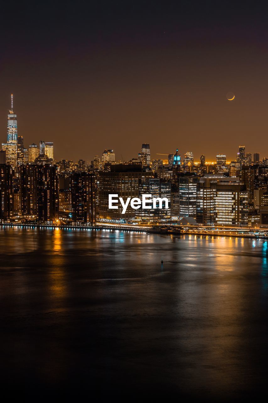 Illuminated buildings by river against sky at night