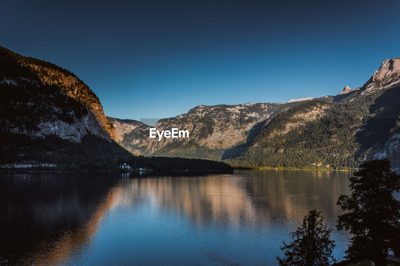 Scenic view of lake and mountains against clear blue sky