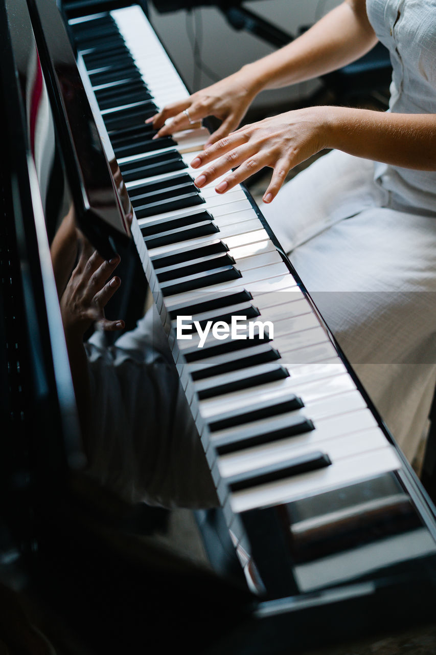 Crop anonymous female musician playing piano while practicing at home at weekend