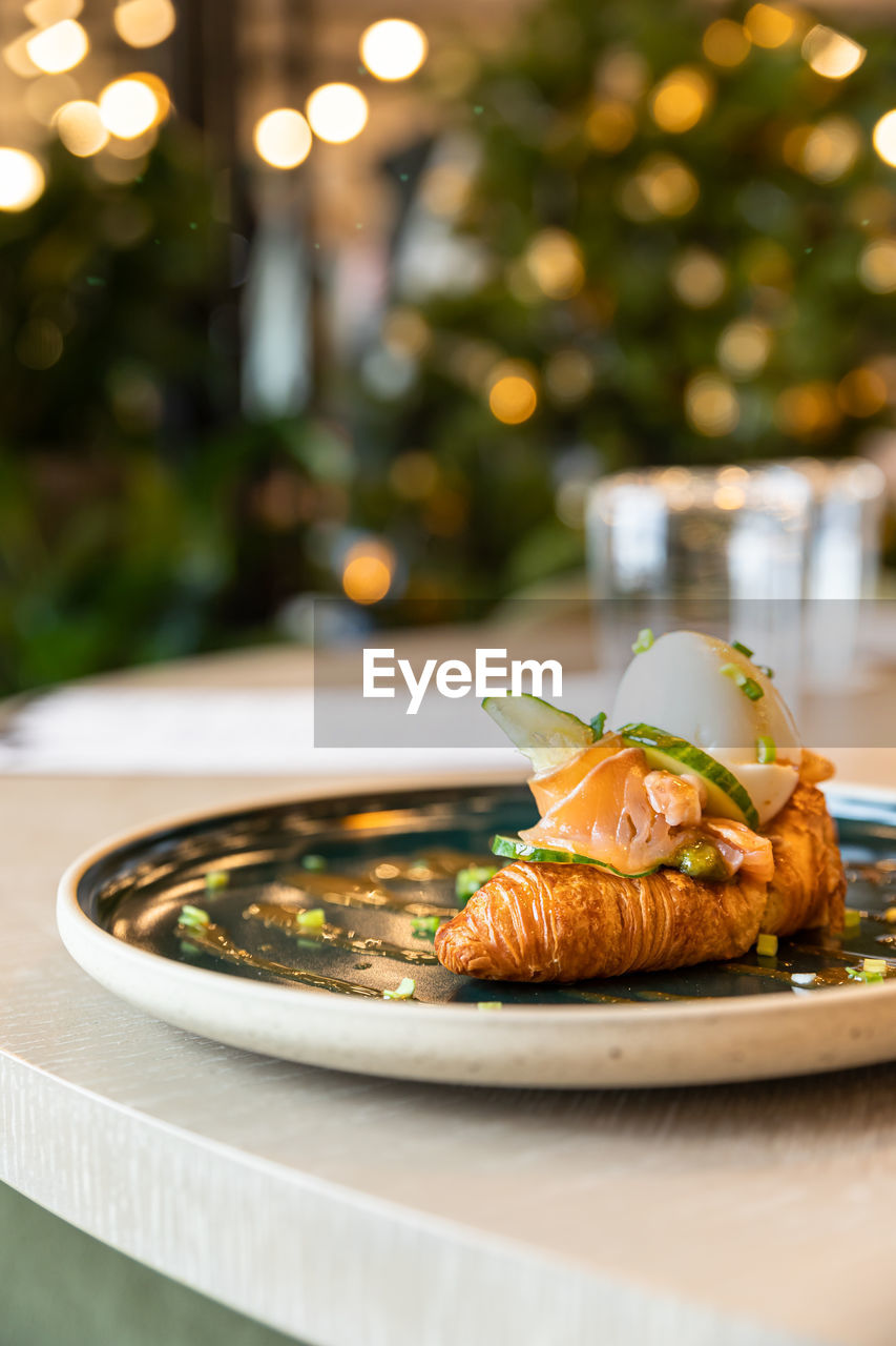 Croissant sandwich with salmon, egg and cucumber. breakfast in cafe or coffee shop. lifestyle.