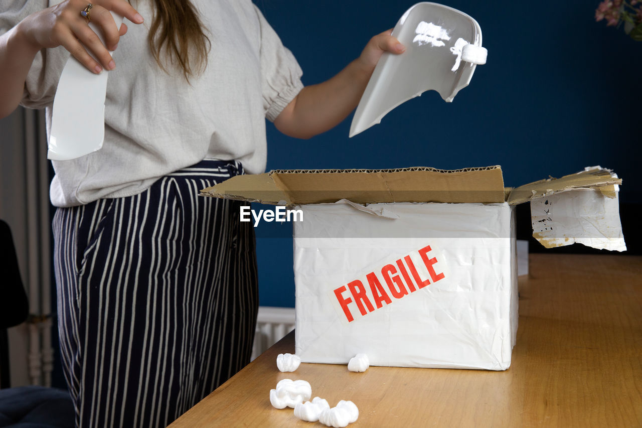 MIDSECTION OF WOMAN HOLDING PAPER WHILE STANDING ON BOX