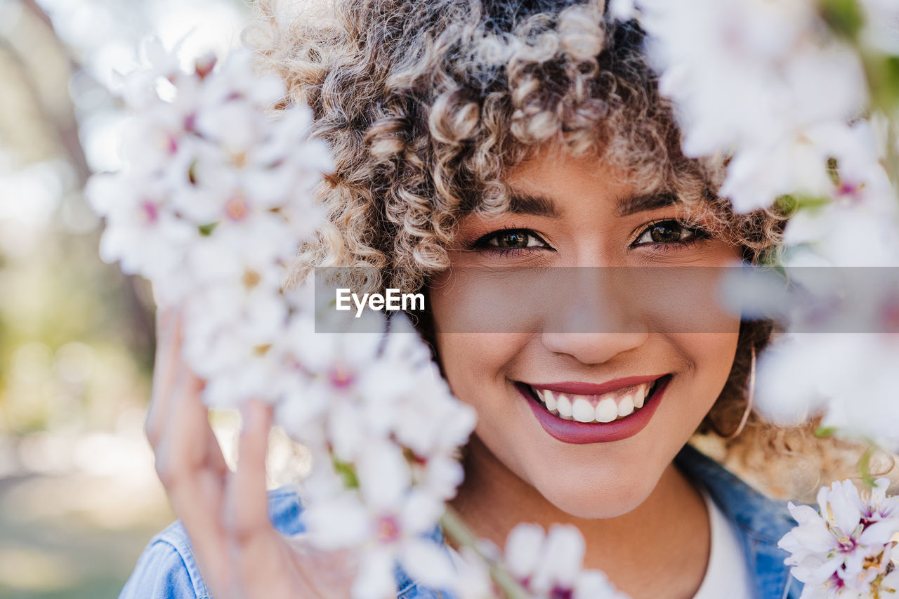 Portrait of happy hispanic woman with afro hair in spring among pink blossom flowers. nature