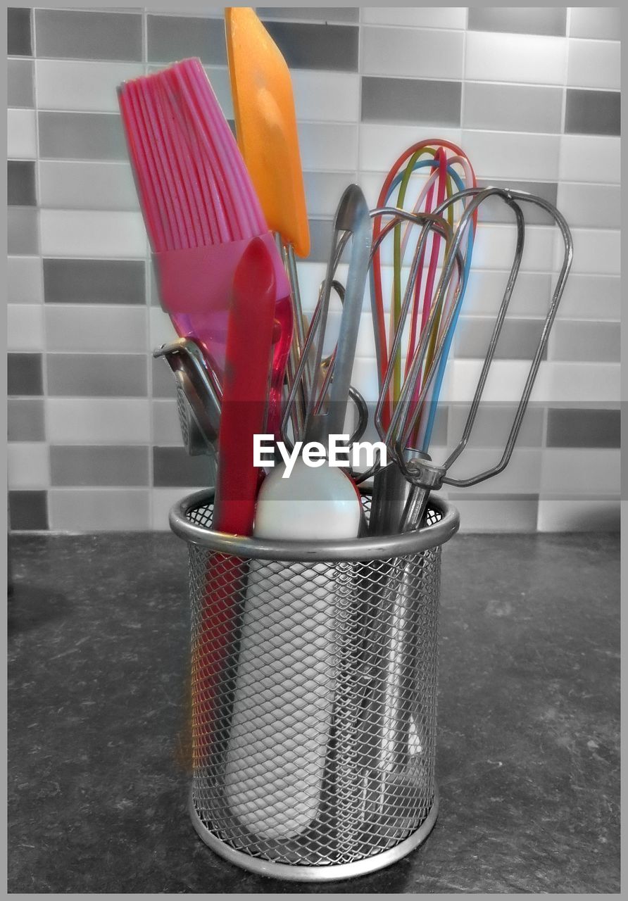 Close-up of cooking utensils in container against tiled wall