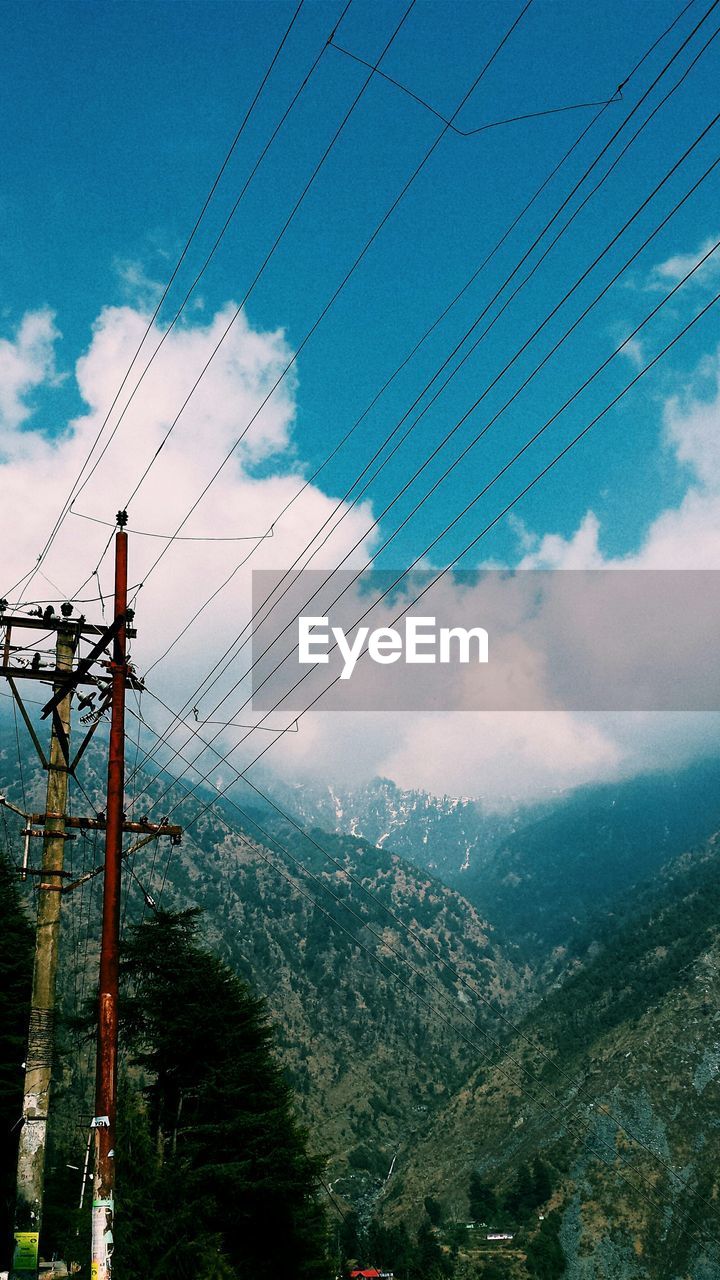 Electric pylon on hills against cloudy sky