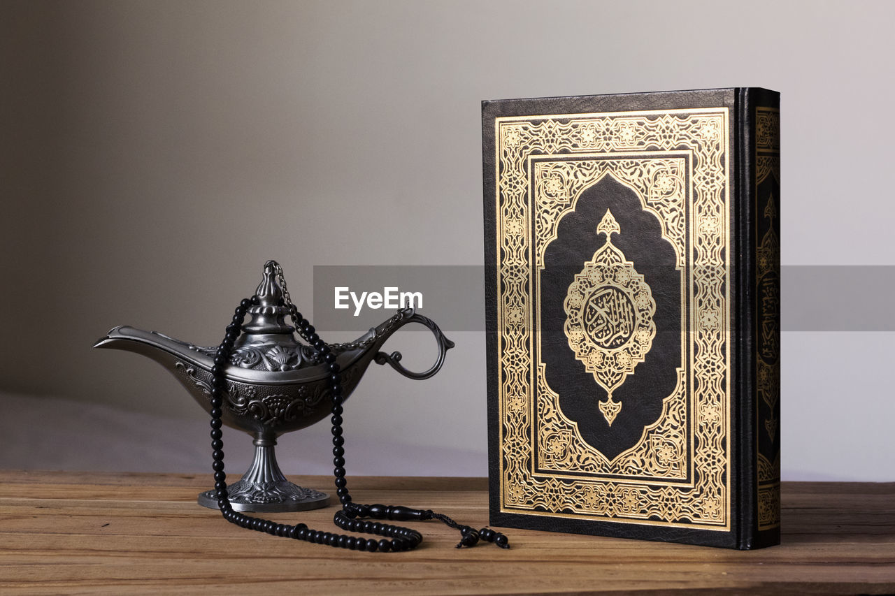 High angle view of koran and bead necklace with magic lamp on table