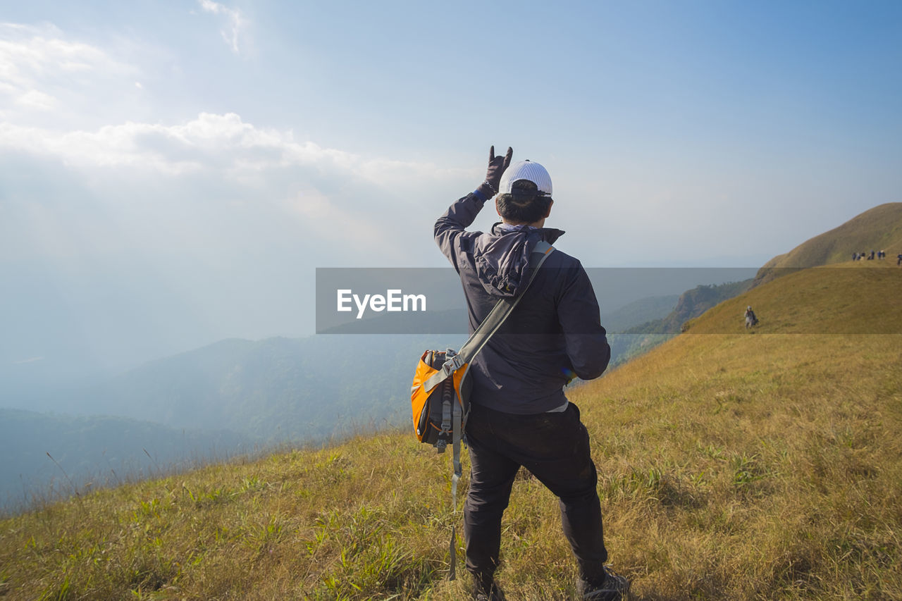 Rear view of hiker showing horn sign on mountain against sky