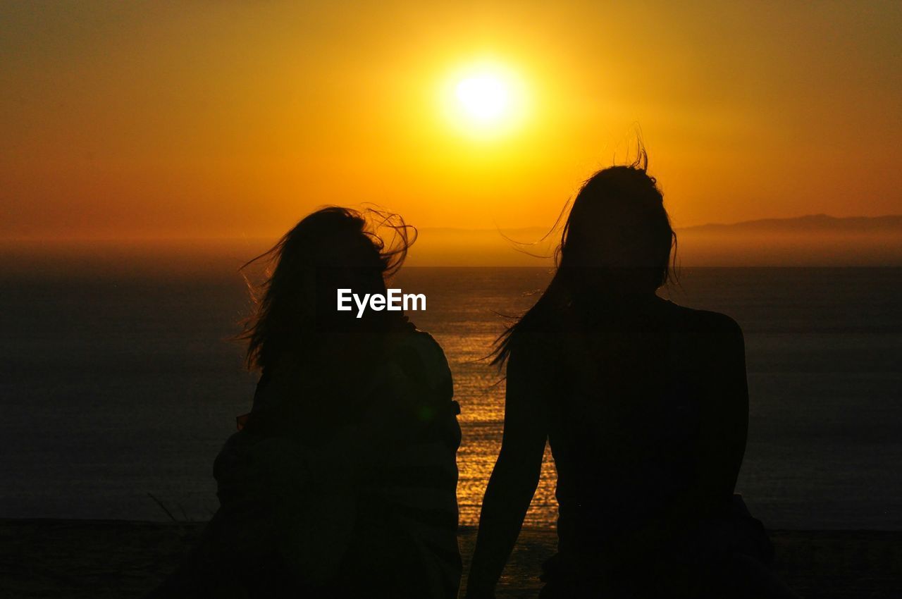 Rear view of silhouette women against sky at beach during sunset
