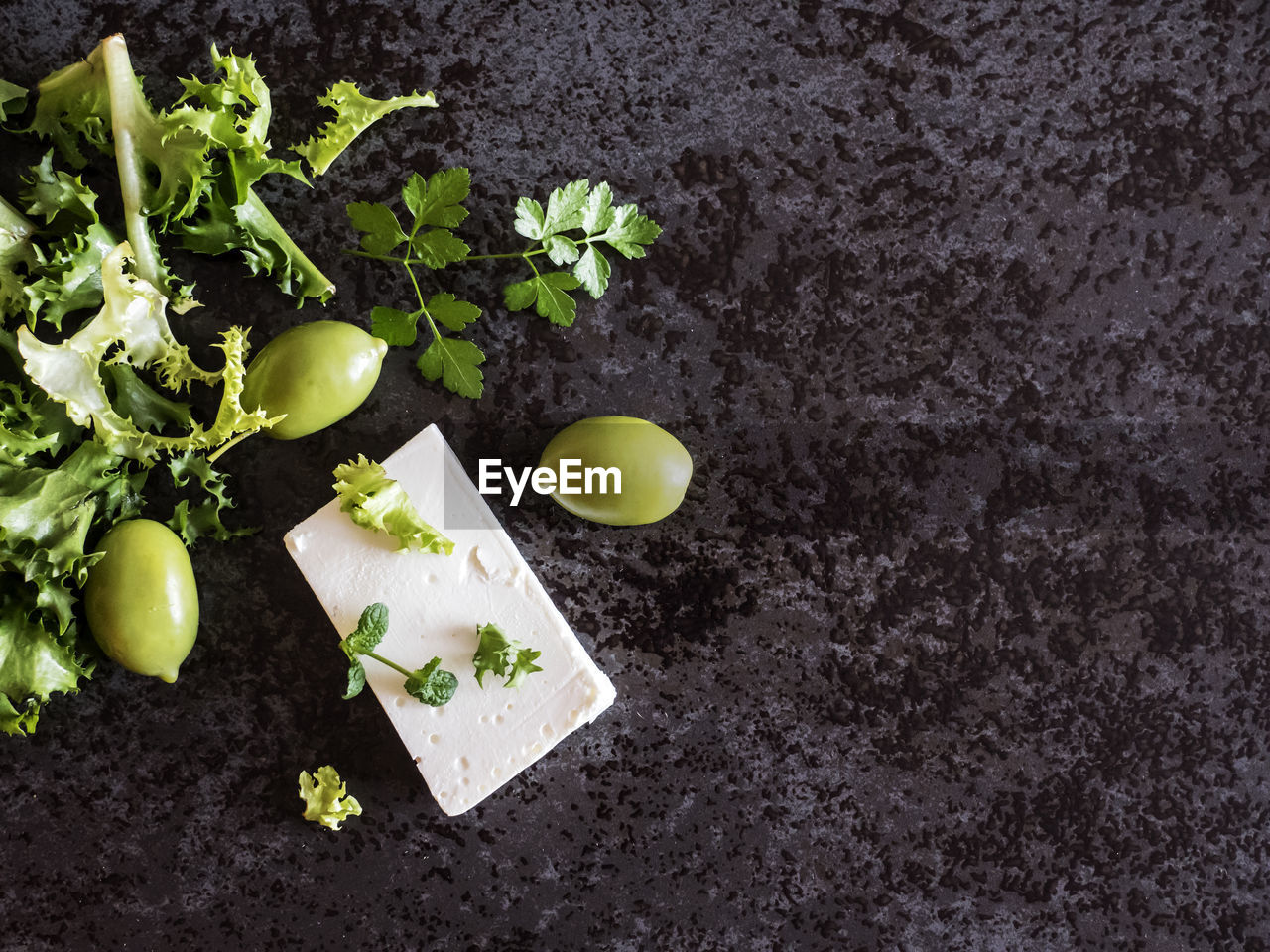 High angle view of feta cheese with olives and green herbs on marble counter