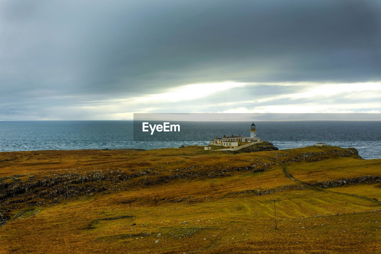 Lighthouse at shore against cloudy sky