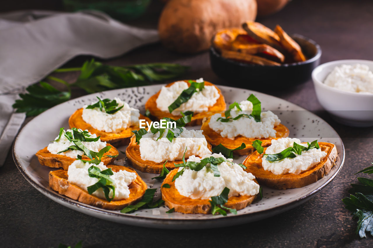 Pieces of baked sweet potato with ricotta and herbs on a plate on the table