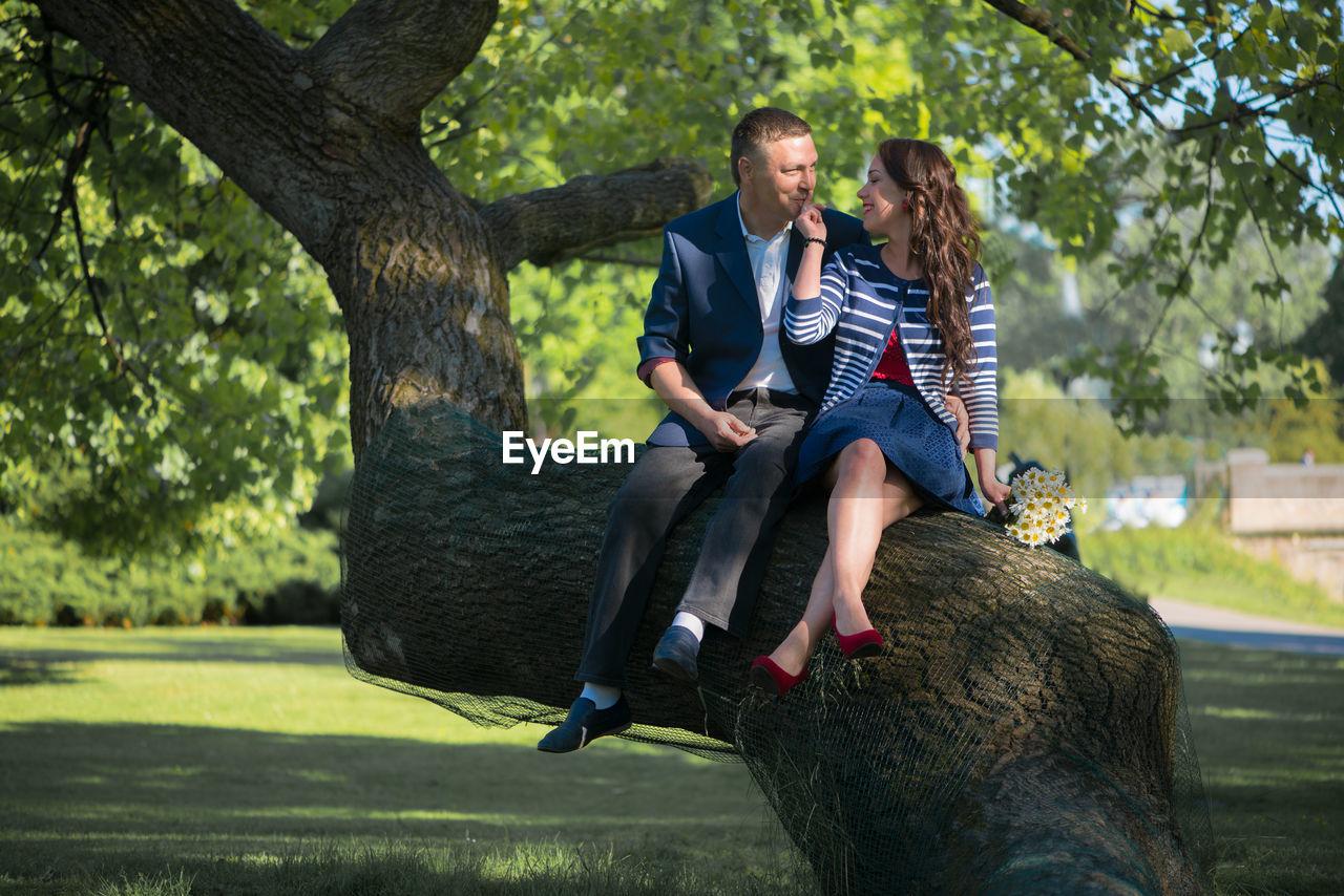 Man and woman sitting on tree trunk at park