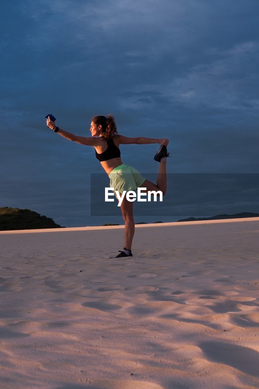 Woman making yoga pose at sunset in sand dunes