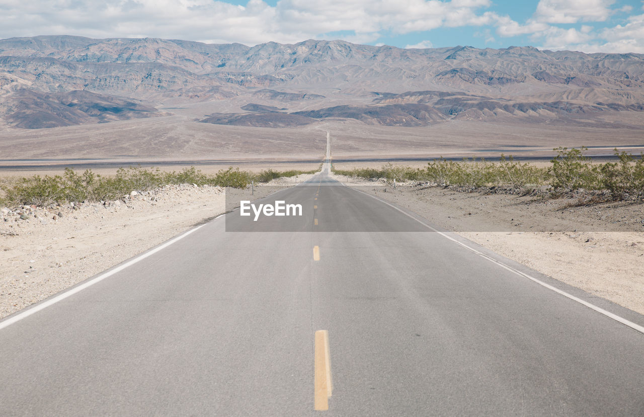 Empty road amidst field leading towards mountains