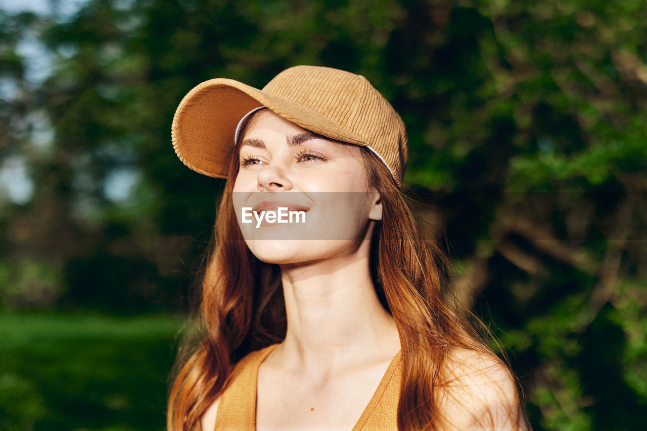 portrait of young woman wearing hat standing against plants