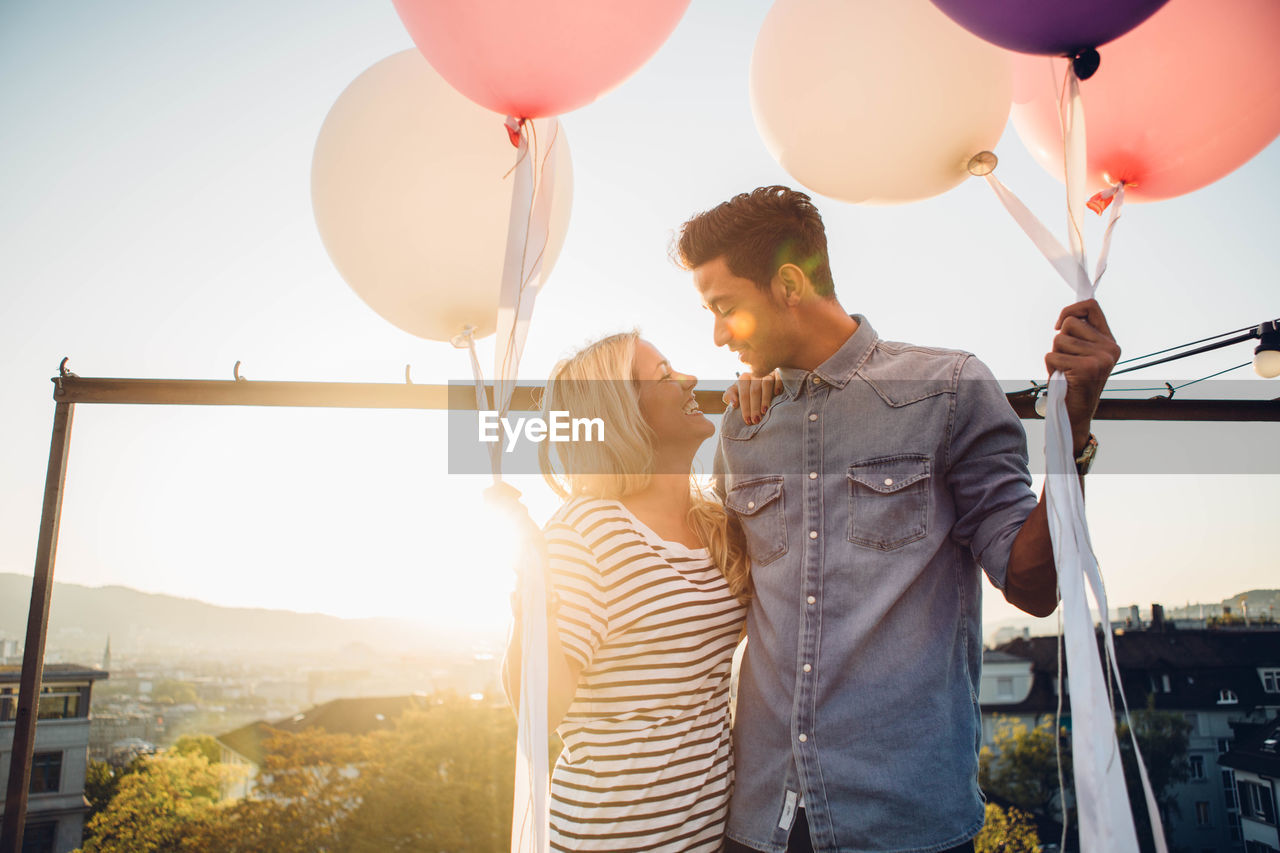 Couple standing with balloons against sky