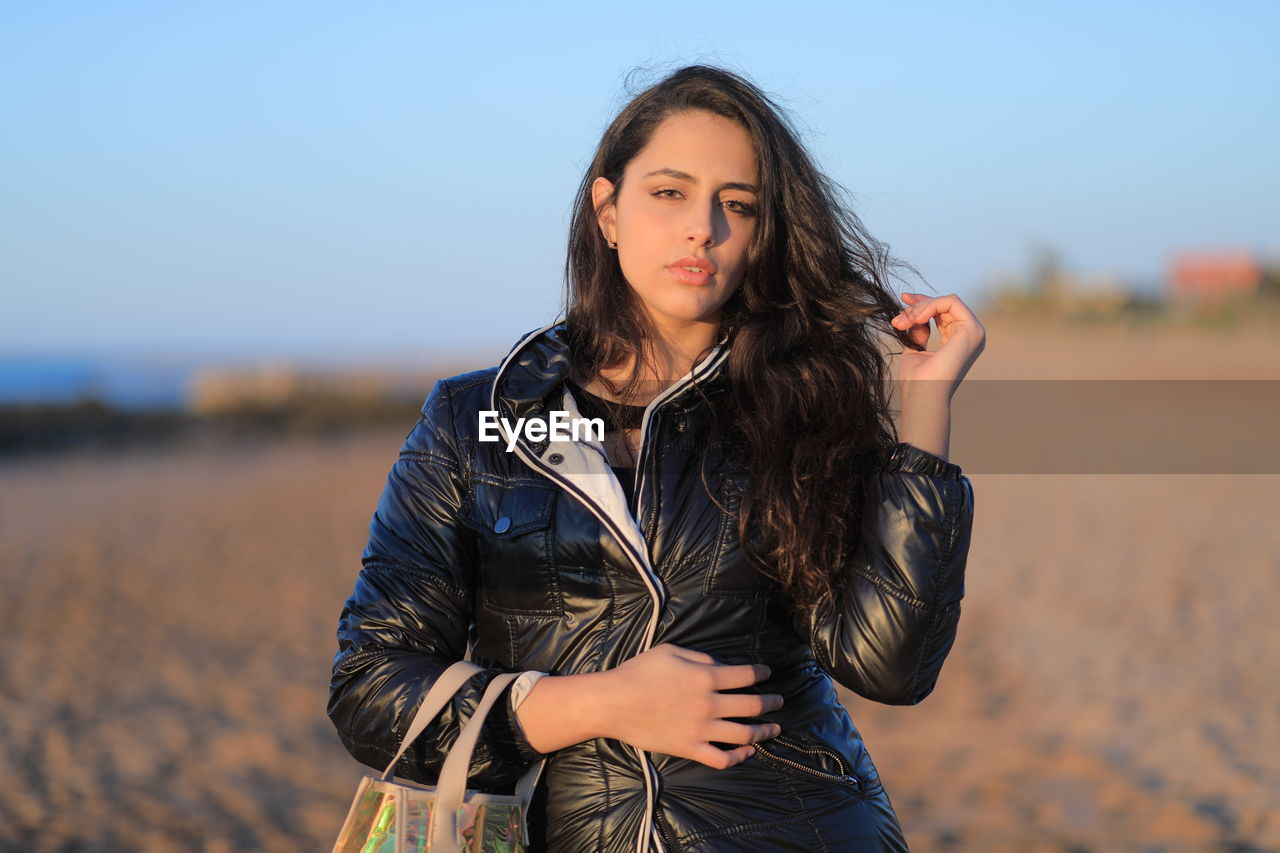 Portrait of beautiful woman standing at beach against sky