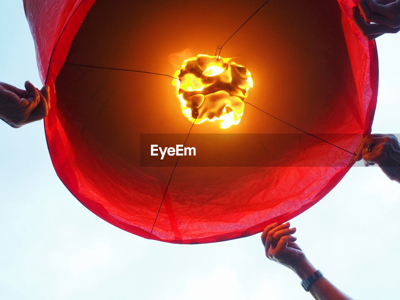 Cropped hands holding lit red paper lantern against clear sky