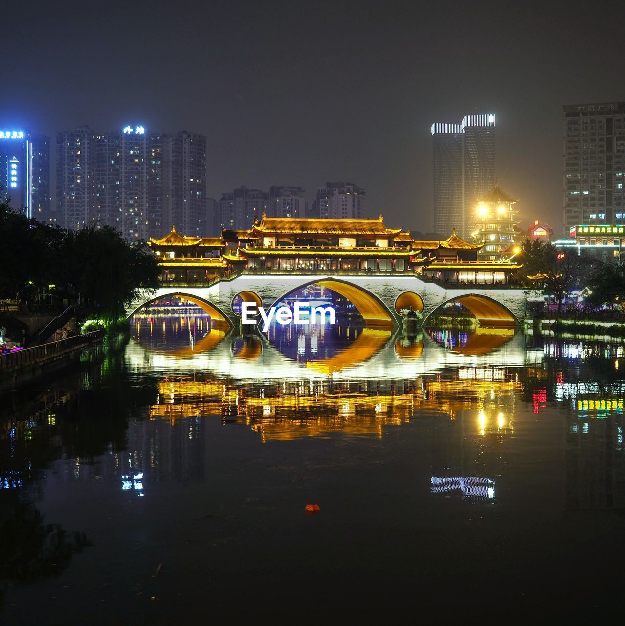 ILLUMINATED MODERN BUILDING BY RIVER AGAINST SKY AT NIGHT