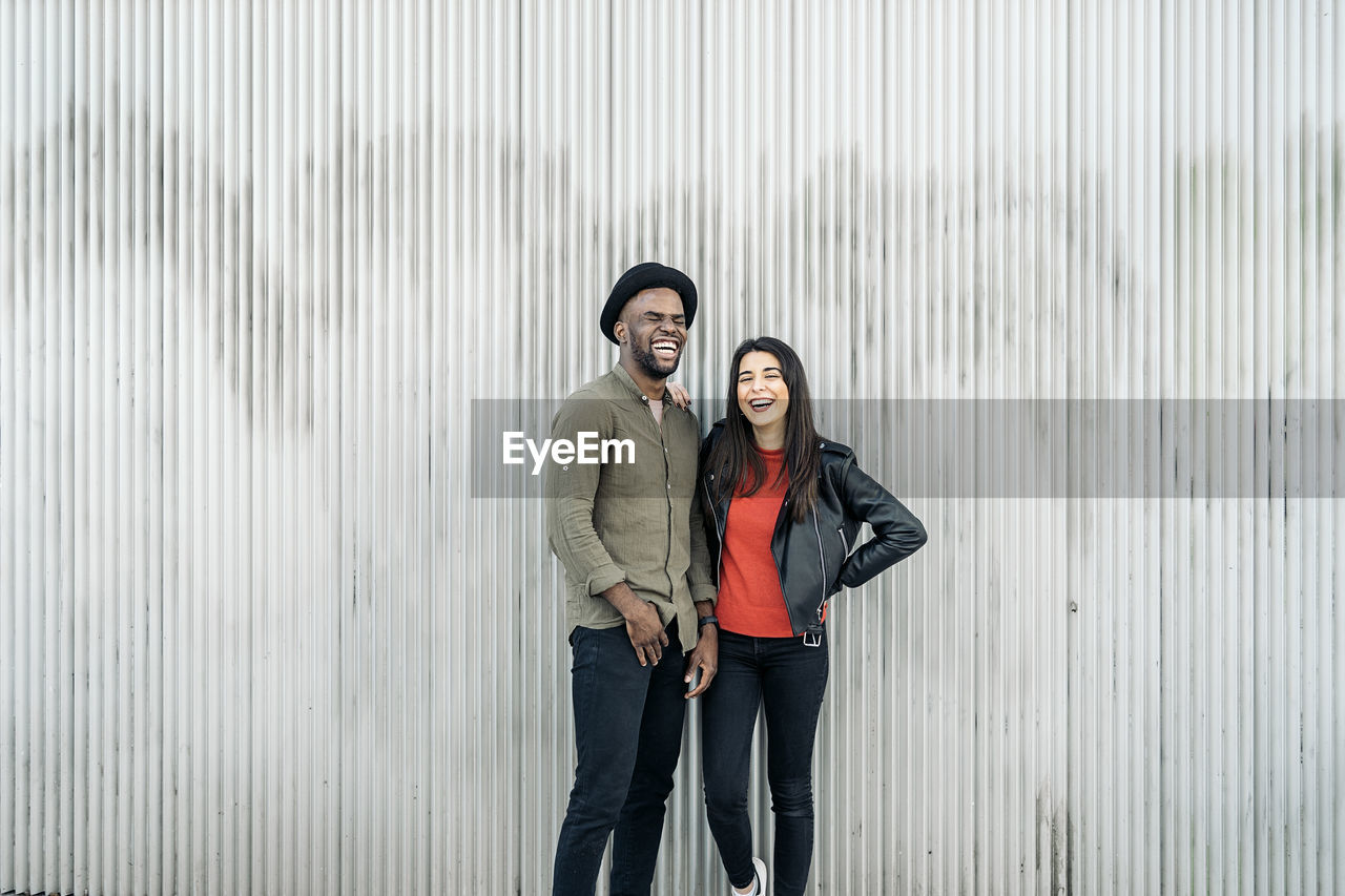 Laughing young couple standing against wall