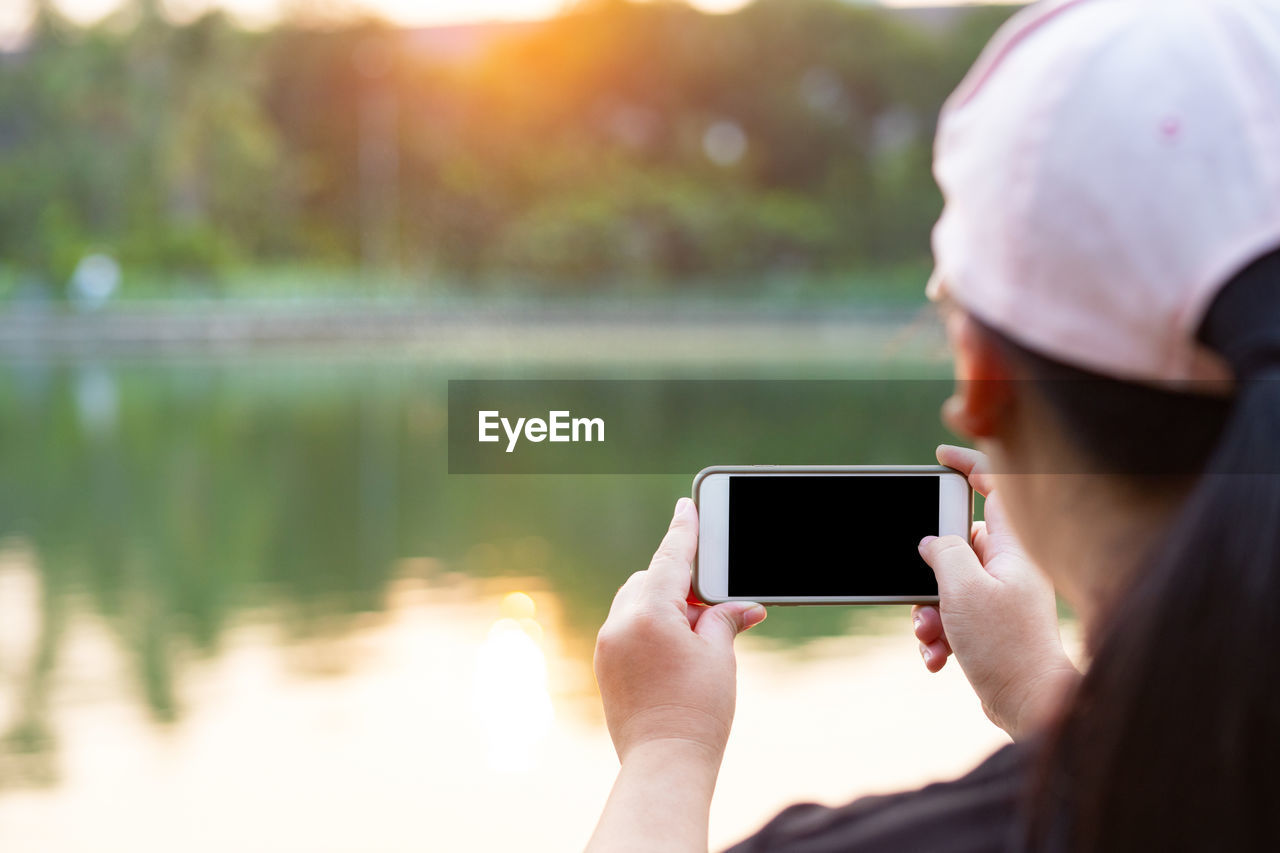 MIDSECTION OF MAN USING MOBILE PHONE WHILE STANDING BY LAKE